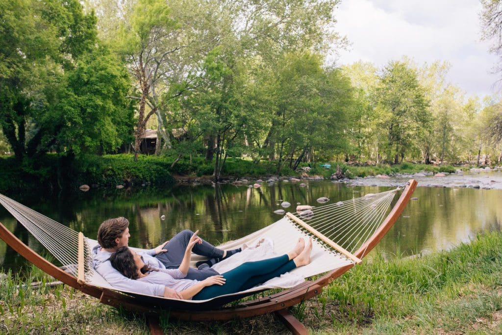 A couple laying in a hammock together along the river at L’Auberge de Sedona.