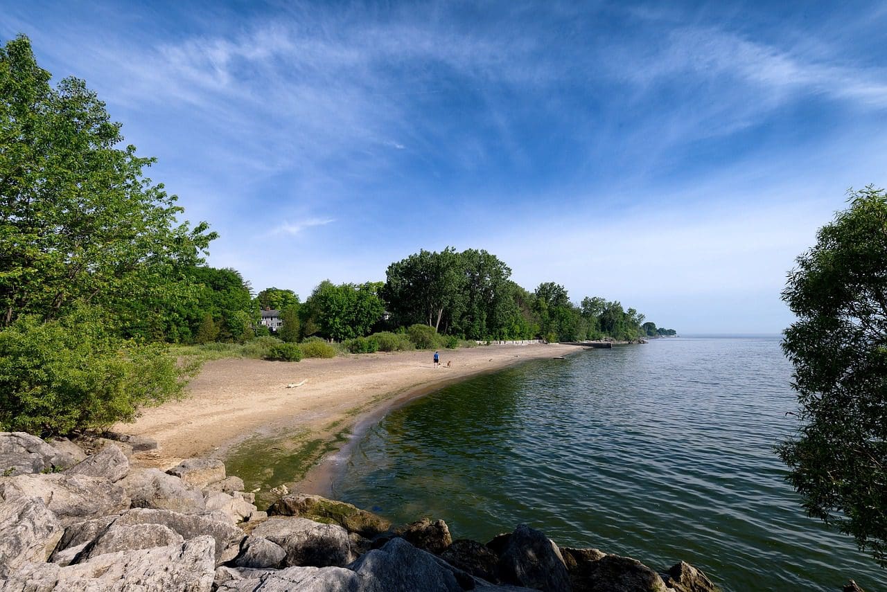 A view of Lake Ontario, including a small beach, on a sunny day, one of the best lakes in New York State for families.