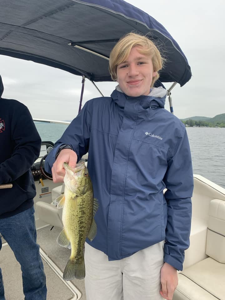 A teen boy holds up a fish he caught from a boat on Lake George, one of the best lakes in New York State for families.