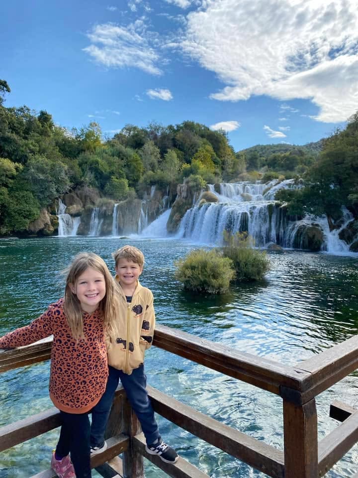 Two kids smile broadly on a viewing platform overlooking a waterfall in Krka National Park near Šibenik.