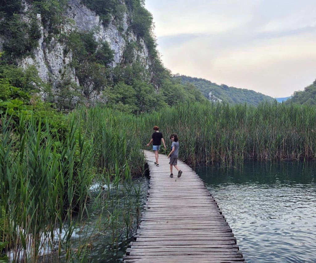 A family walks across a boardwalk train in Plitvice Lakes National Park, one of the best places to visit in Croatia with kids this summer.