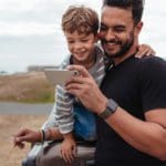 A dad and his young son watch a travel video on a smart phone.