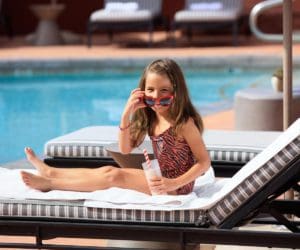 A young girl with sunglasses enjoys a sunny day at the hotel pool.