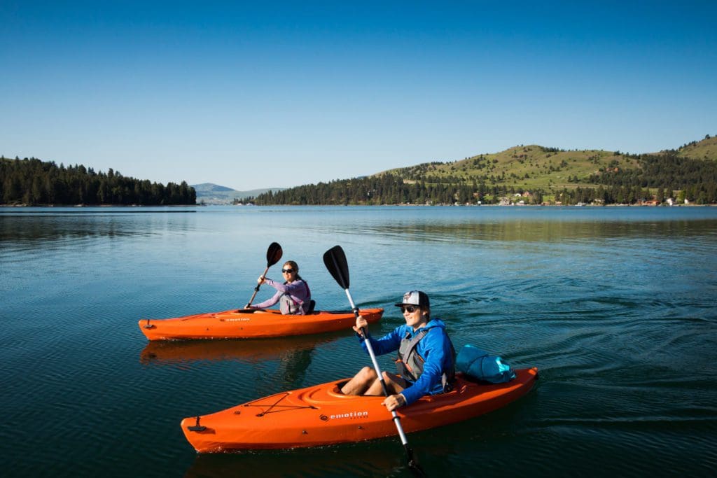 Two kayakers enjoy a sunny day paddling around the water in Montana.