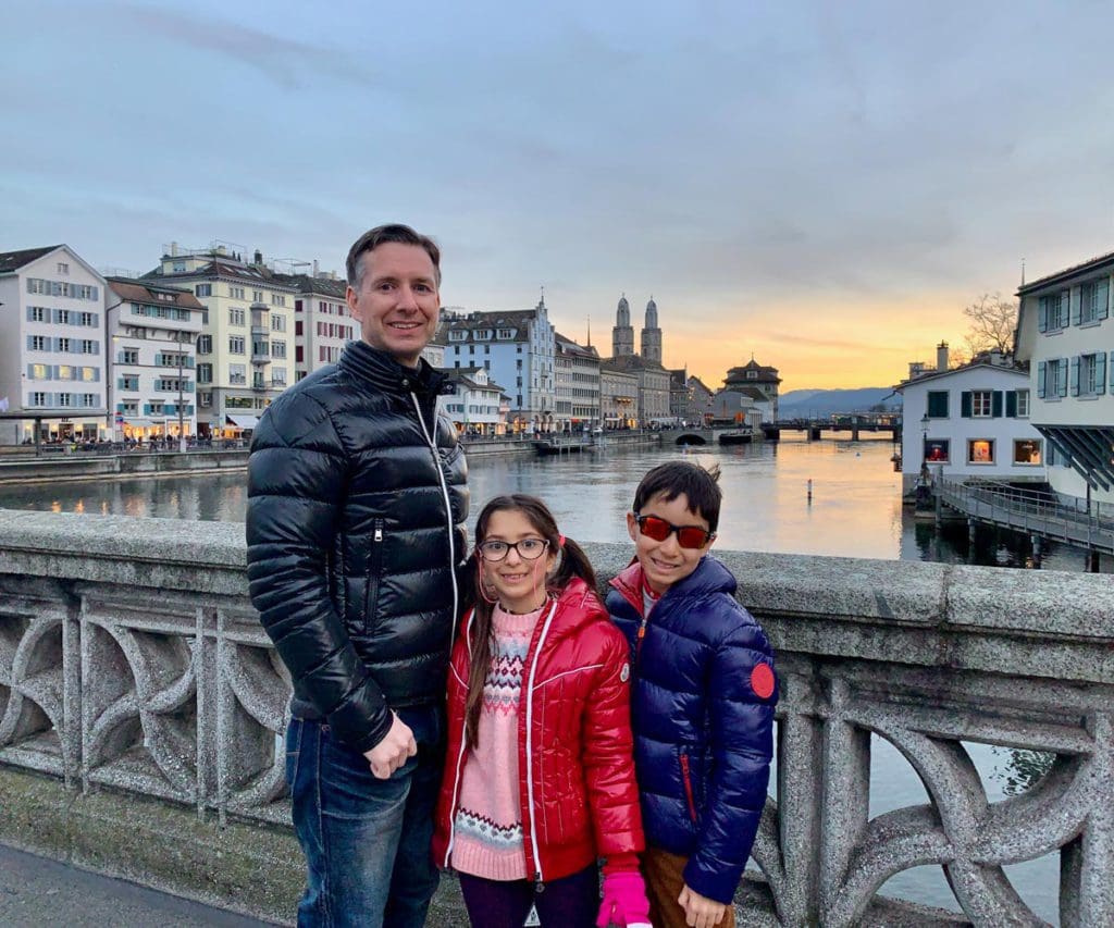 A dad and his two young kids stand on a bridge in Zurich at sunset.