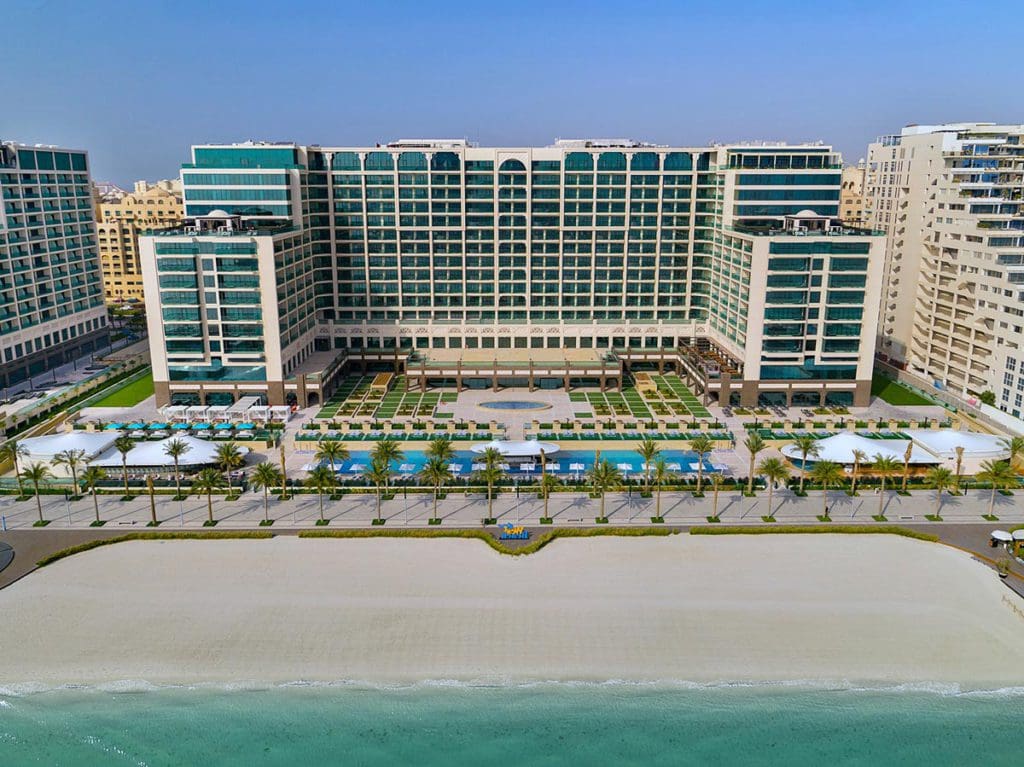 The exterior of Hilton Dubai Palm Jumeirah along a large beach, one of the best beachfront hotels in Dubai for families.