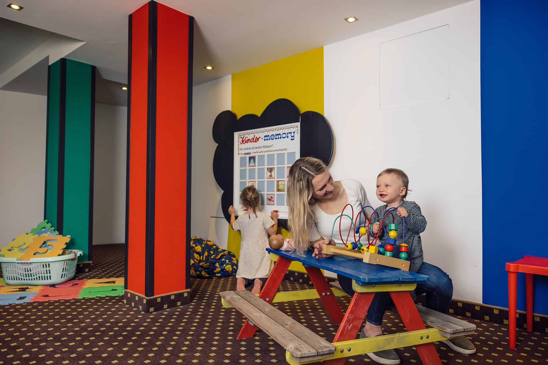 The colorful kids' play area in Hotel Bon Alpina, with a mom and her two kids playing together.