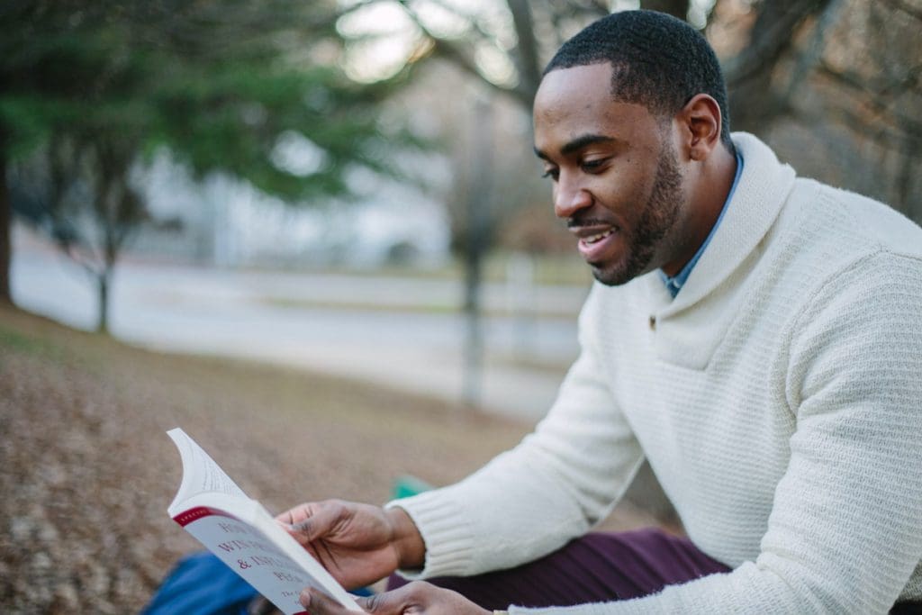A black man reads a book in a park.