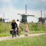 A family of three bikes past windmills in the Netherlands.