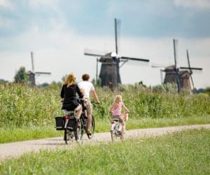A family of three bikes past windmills in the Netherlands.