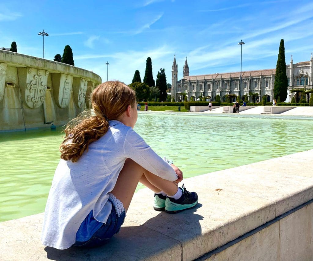 A young girl sits along Belem Fountain, a fun stop on any Lisbon itinerary with kids.