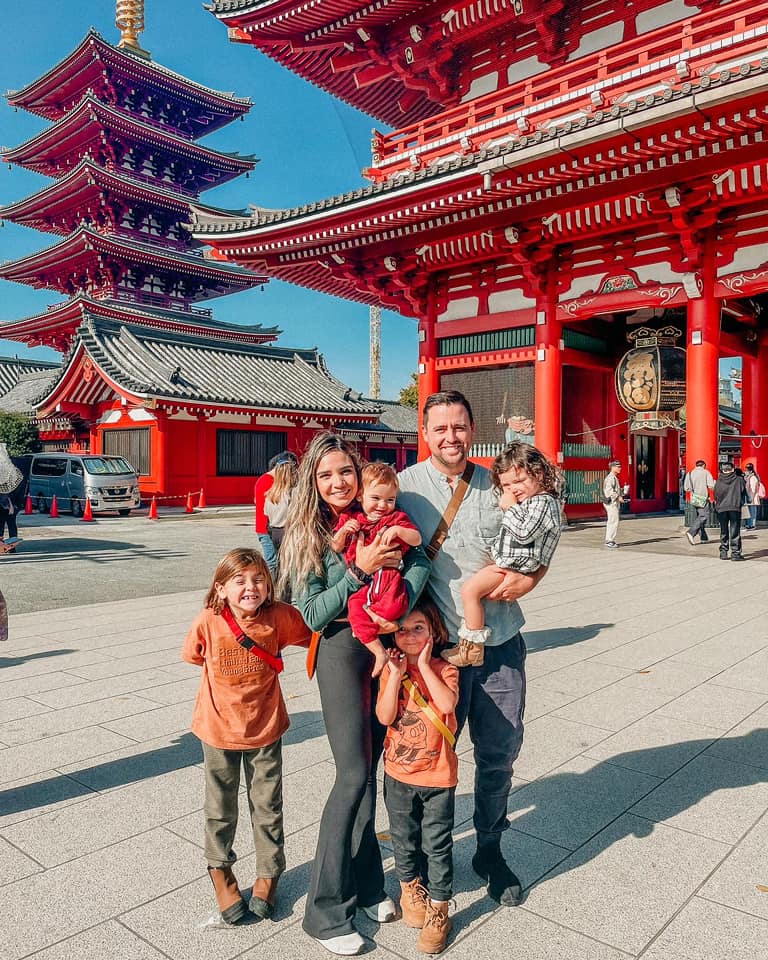 A family of five stands together in front of a temple in Tokyo, one of the best places to visit with kids in 2024. 