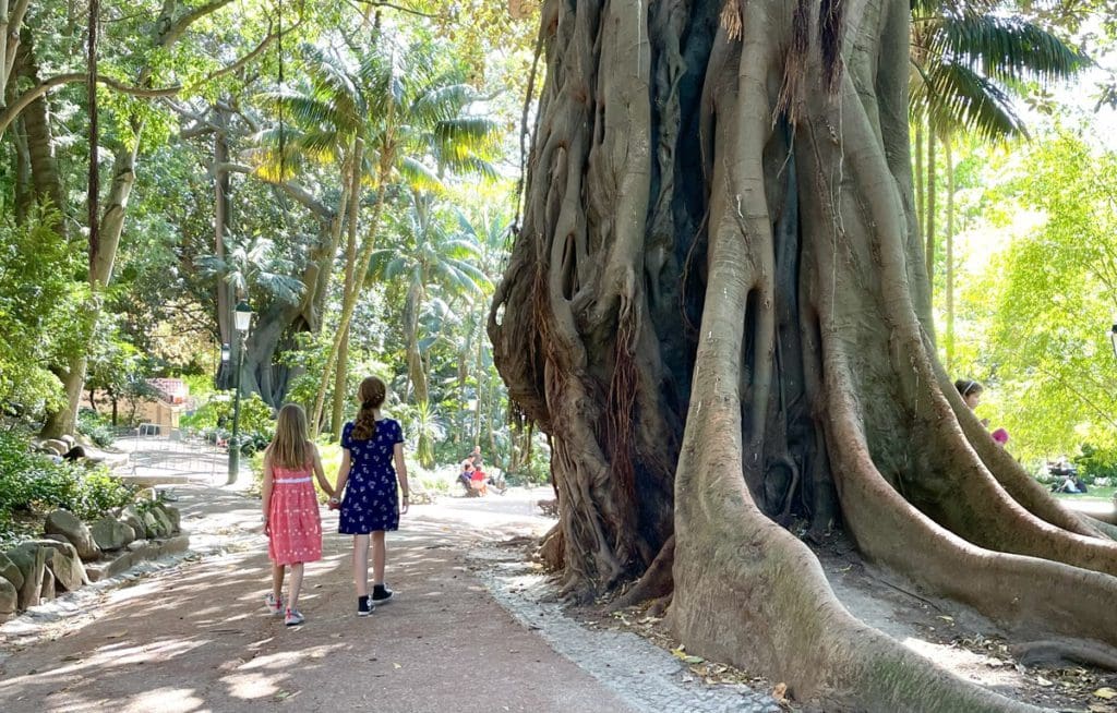 Two young girls walk hand-in-hand while exploring Jardim da Estrela, a fun stop on any Lisbon itinerary with kids.