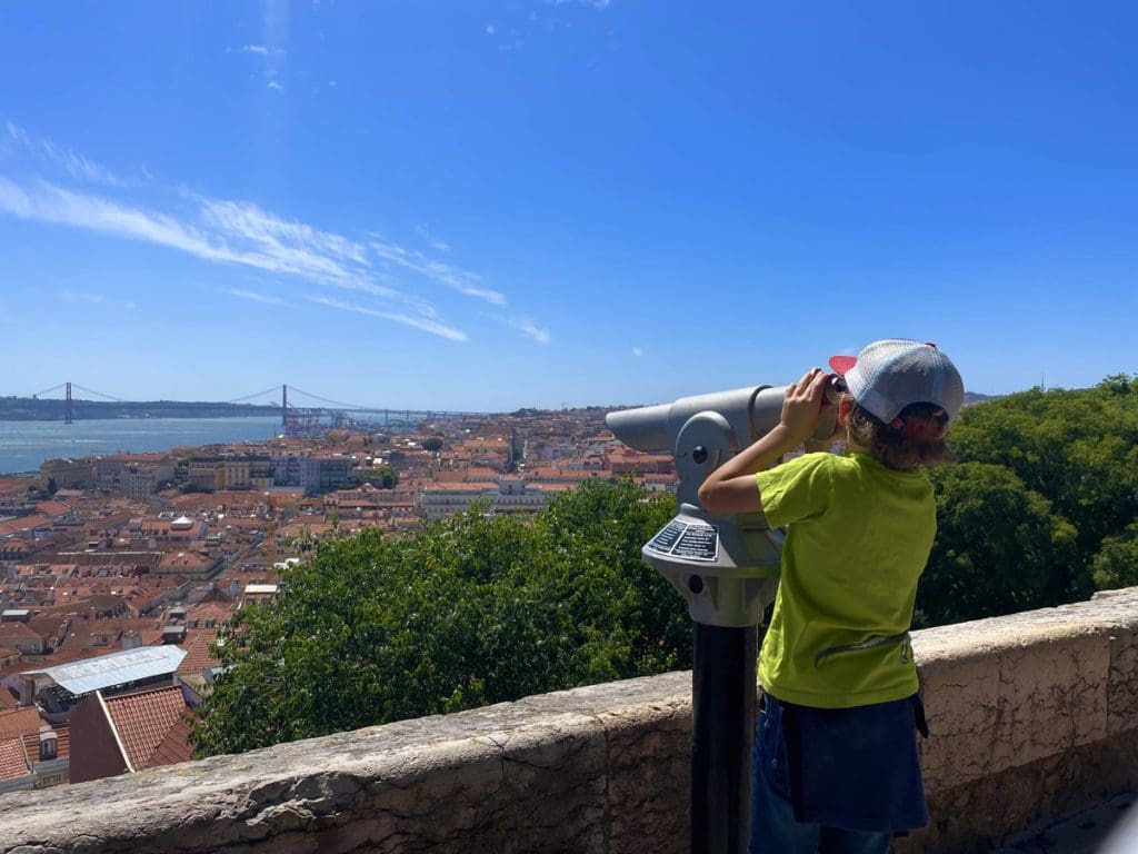 A young boy looks through a spy scope at Largo Santa Luiza, a fun stop on any Lisbon itinerary with kids.