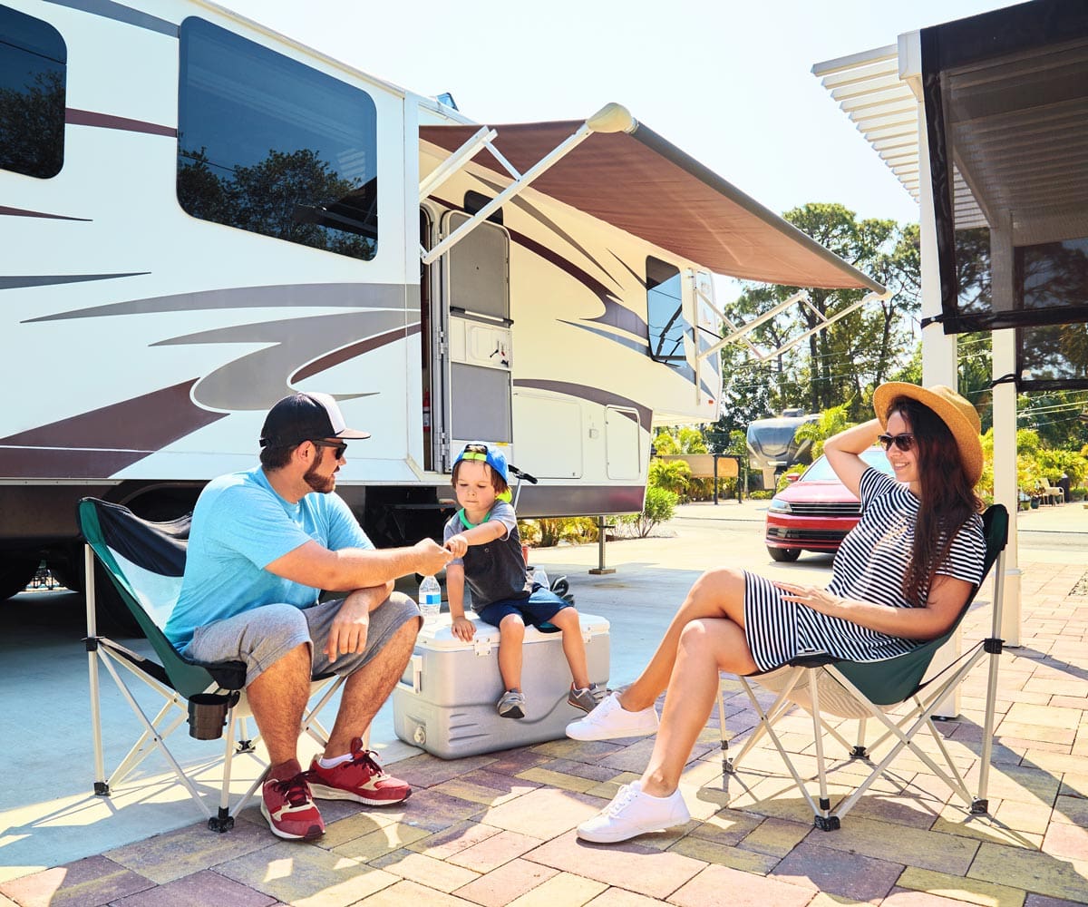 A family of three sits together outside their RV.