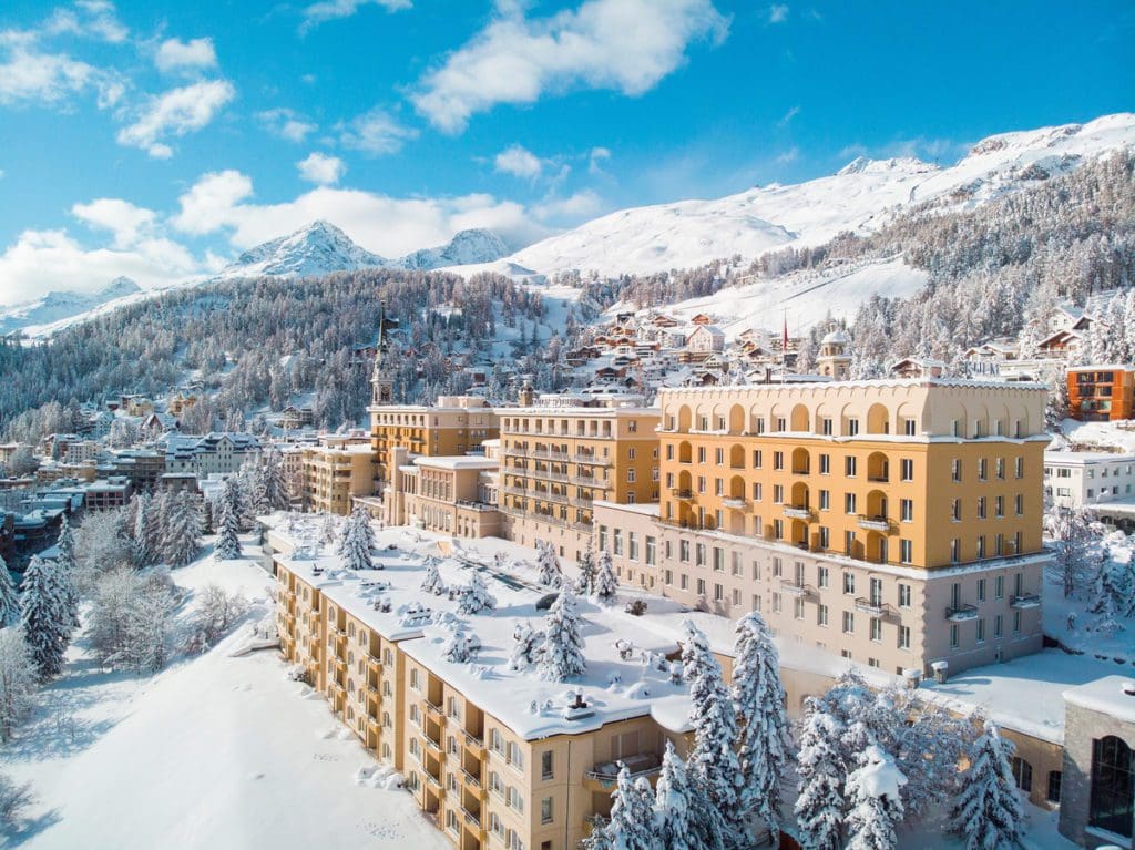 Kulm Hotel St. Moritz covered in snow, with snowcapped mountains in the distance, one of the best hotels in St. Moritz for families.