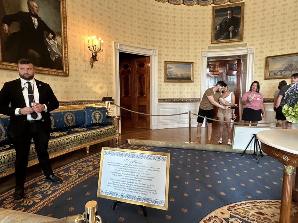 People on tour at the White House, with a serviceman watching over the room.
