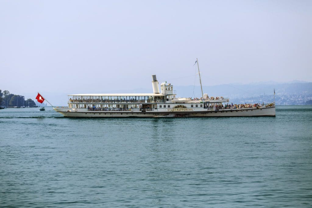 A boat moves along the waters of Lake Zurich, carrying tourists enjoying a sunny day.