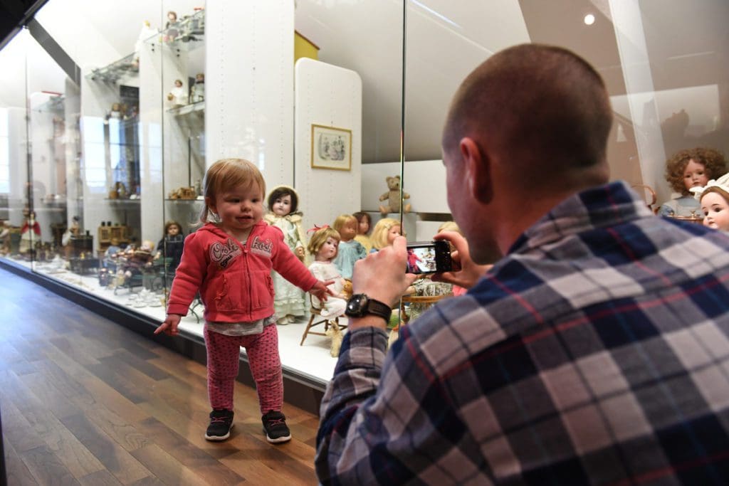A dad takes a picture of his toddler daughter while they explore the Zürcher Spielzeugmuseum.