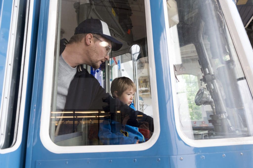 A young boy and his dad sit in the driver's seat of a tram at the Zürich Tram Museum.