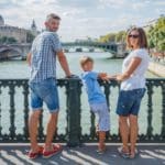 A family of three stands together along the River Seine in Paris.
