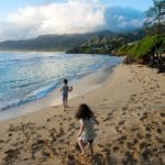 Two kids run along a beach in Hawaii on a sunny day.