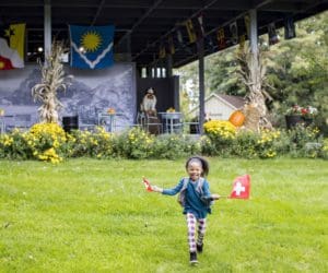 A young girl runs through a grassy area waving Swiss flags near a museum in New Glarus, Wisconsin.