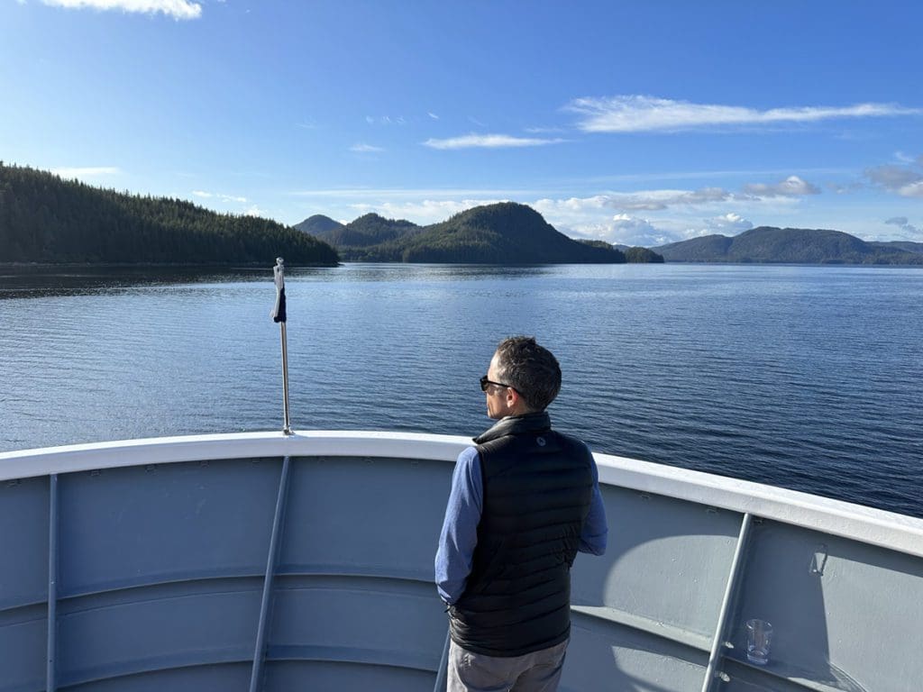 A man stands at the bow of a cruise ship looking toward the shoreline of Alaska, a must on any Alaska itinerary for families by sea.