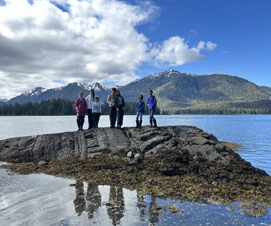 A family stands on a rock outcropping in the water, off-shore from Alaska, hiking is a must-do on any Alaska itinerary for families.