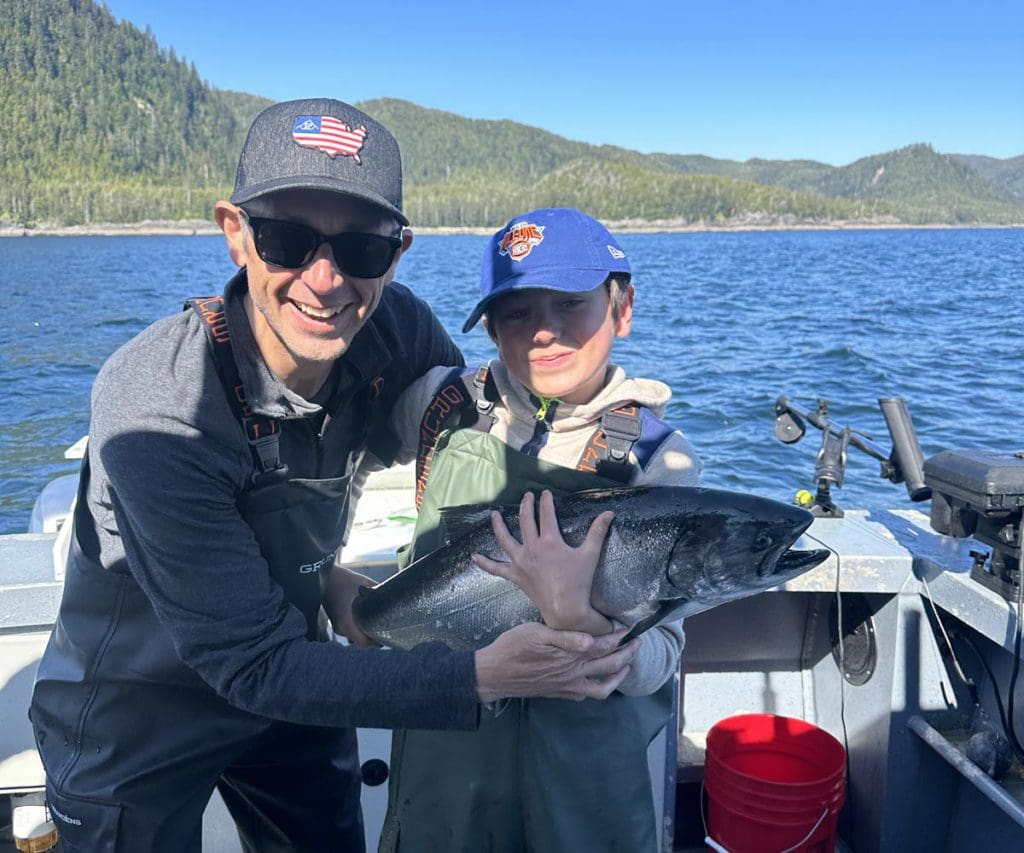 A dad and his son hold a fish they caught in Alaska.