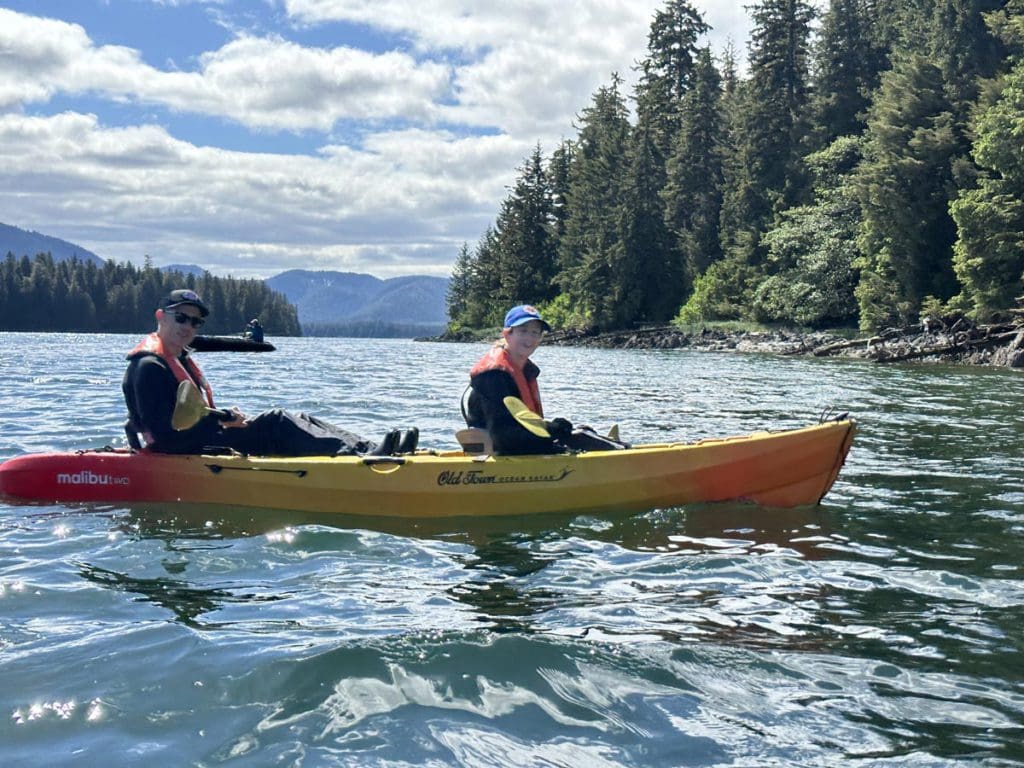 A tandem kayak with two people enjoy the water, off-shore from Alaska, a must-do activity on any Alaska itinerary for families.