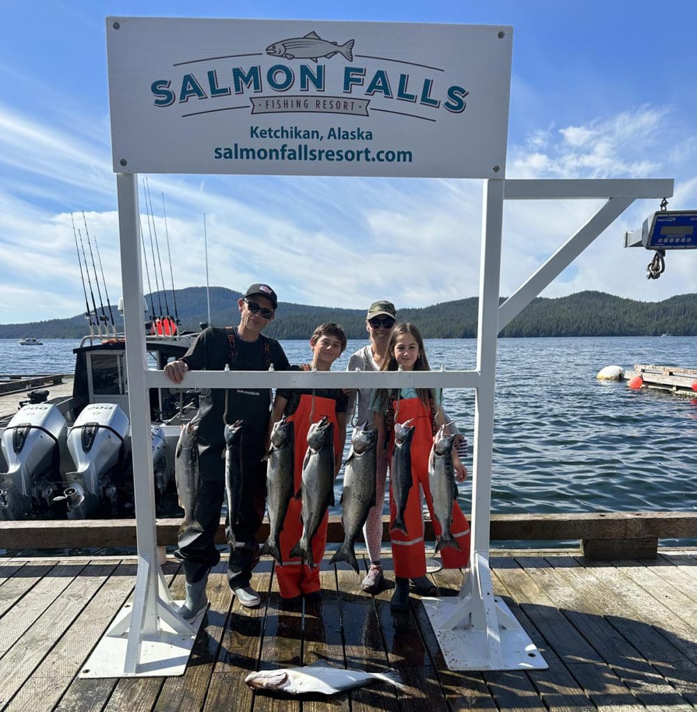 A family stands together behind the salmon they caught in Alaska, a must-do on any Alaska itinerary for families.