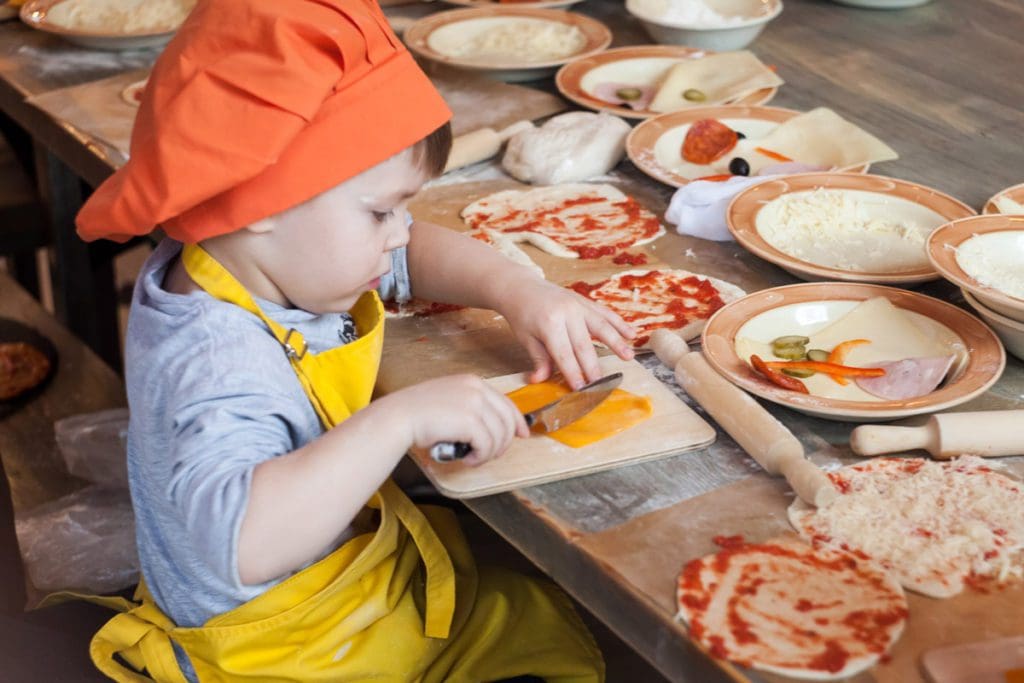 A young boy makes pizza through a cooking class in Tuscany, one of the best tours and classes in Tuscany with kids.