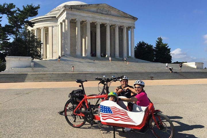 A family of three poses together in front of a monument, while on the Private Family-Friendly DC Tour by Bike.