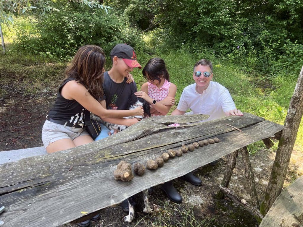 A family of four poses together near all the truffles they found on their truffle hunting class, one of the best tours and classes in Tuscany with kids.