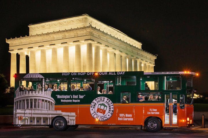 A trolley moves along a Washington DC street at night while leading a Washington DC Monuments by Moonlight Tour by Trolley.