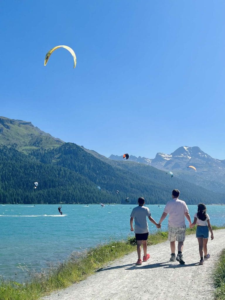 A dad and his twin tweens watch kite-surfers on Lake Silvapana, a fun activity on any St Moritz Itinerary with kids.