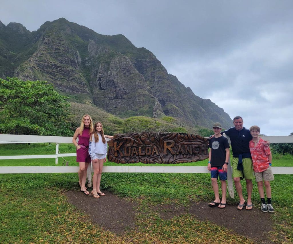 A family poses together at the sign for Kualoa Ranch & Private Nature Reserve.