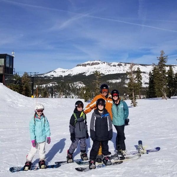A family of five, in ski gear, stands together on a Lake Tahoe mountain run, one of the best things to do while on a ski vacation to Lake Tahoe with kids.