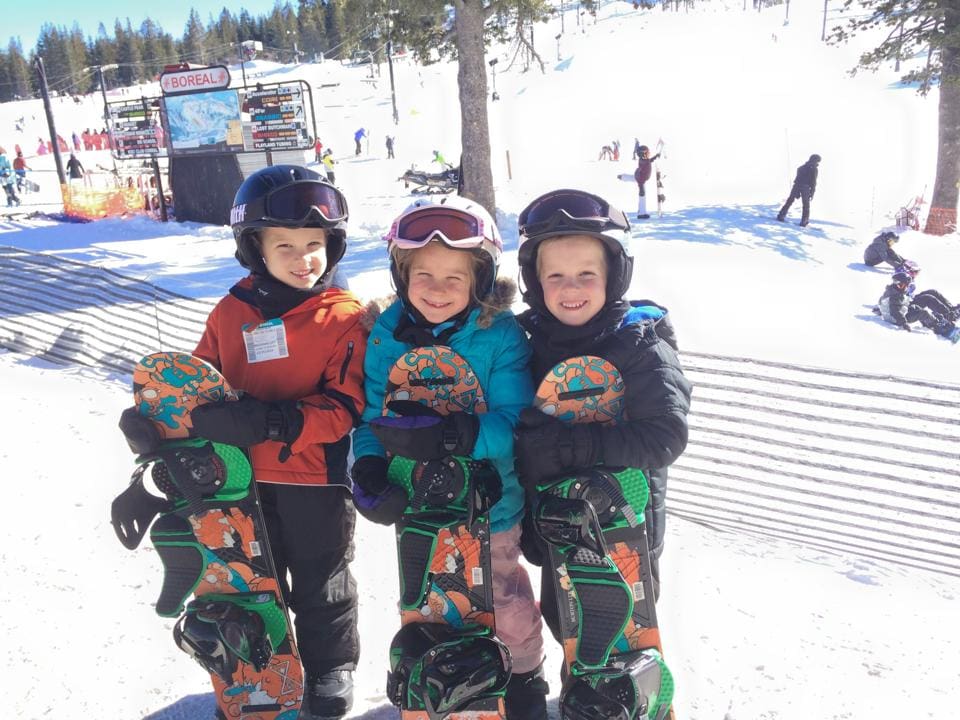 Three young kids stand together with their snowboards at Boreal in Lake Tahoe.