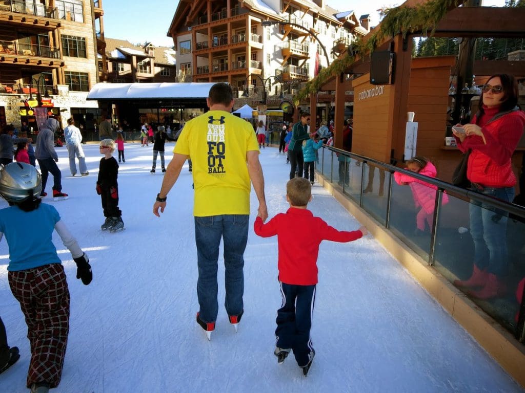A dad and his young son ice skate on a rink in Lake Tahoe, one of the best things to do while on a ski vacation to Lake Tahoe with kids.