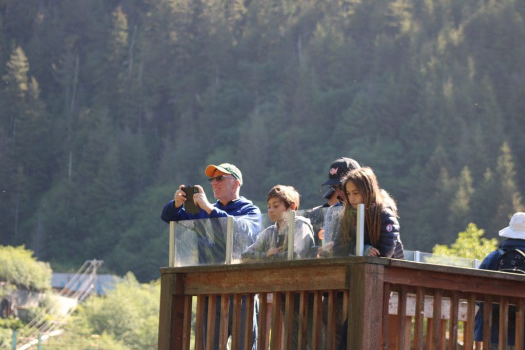 A family stands together from a viewing deck, enjoying a view of the Alaskan wilderness.