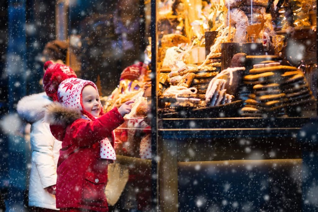 A young child wearing red, looks at treats through a window, while exploring Munich, one of the best destinations for New Year's with kids.