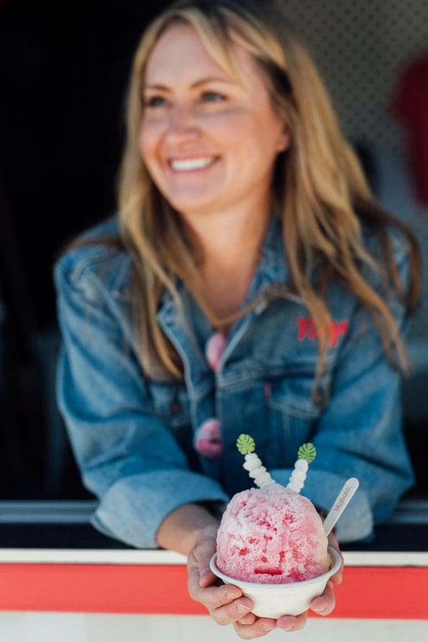 A woman enjoys a pink dessert from Punch Buggy Shave Ice, one of the best dessert spots in Denver with kids.