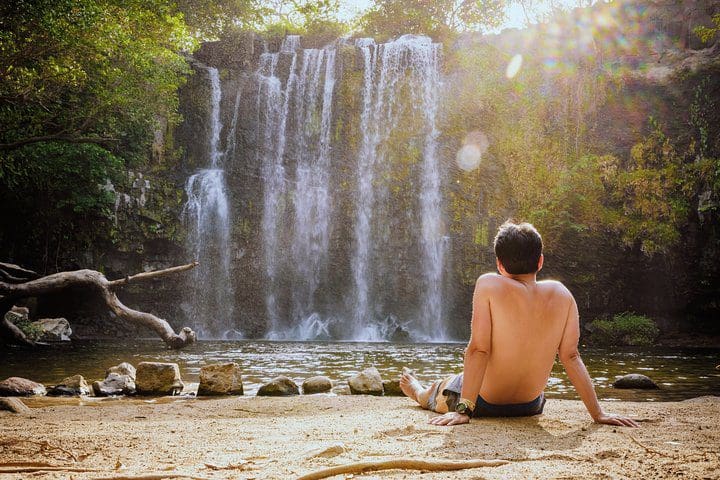 A tourist enjoys a view of a waterfall on the Rio Celeste Hiking, Sloth Sanctuary & Llanos de Cortes Waterfall Tour.