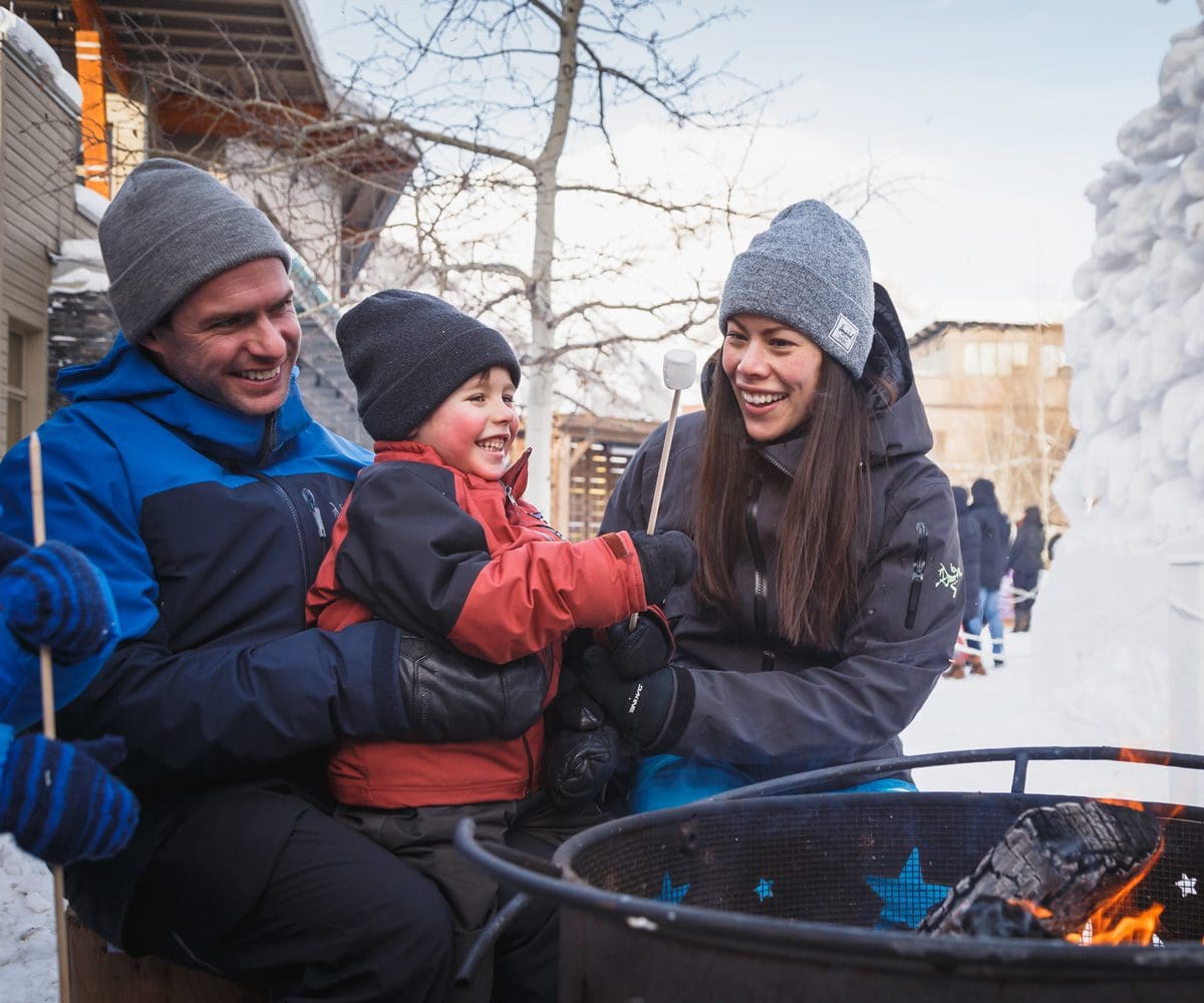 A family of three sits around a winter bonfire in Banff.