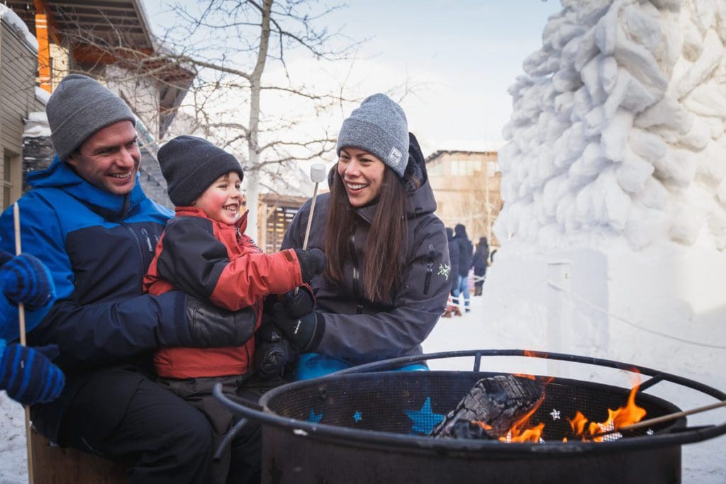 A family of three sits around a winter bonfire in Banff.