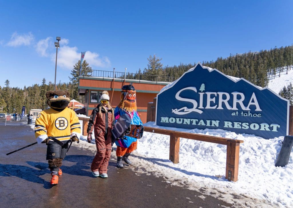 A woman and two mascots walk by the sign for Sierra-at-Tahoe Mountain Resort.