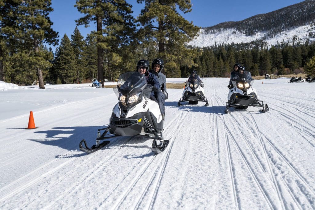 Three snowmobiles carry people across the snow in South Tahoe.
