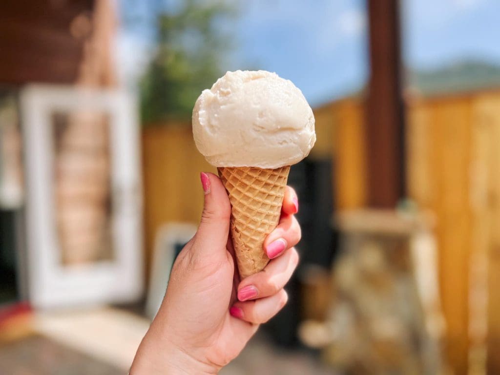 A hand holds out a small ice cream cone in front of the patio area of The Colorado Creamery, one of the best dessert spots in Denver with kids.